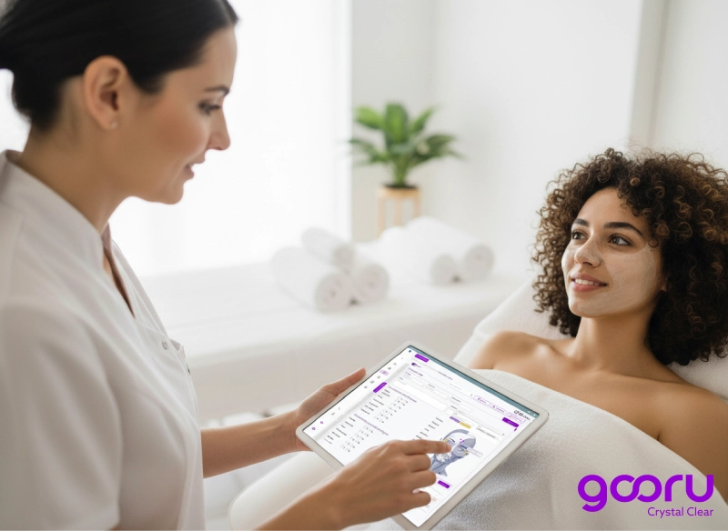 Especialista de spa usando una tablet con Gooru para revisar tratamientos y citas mientras atiende a una paciente en camilla.